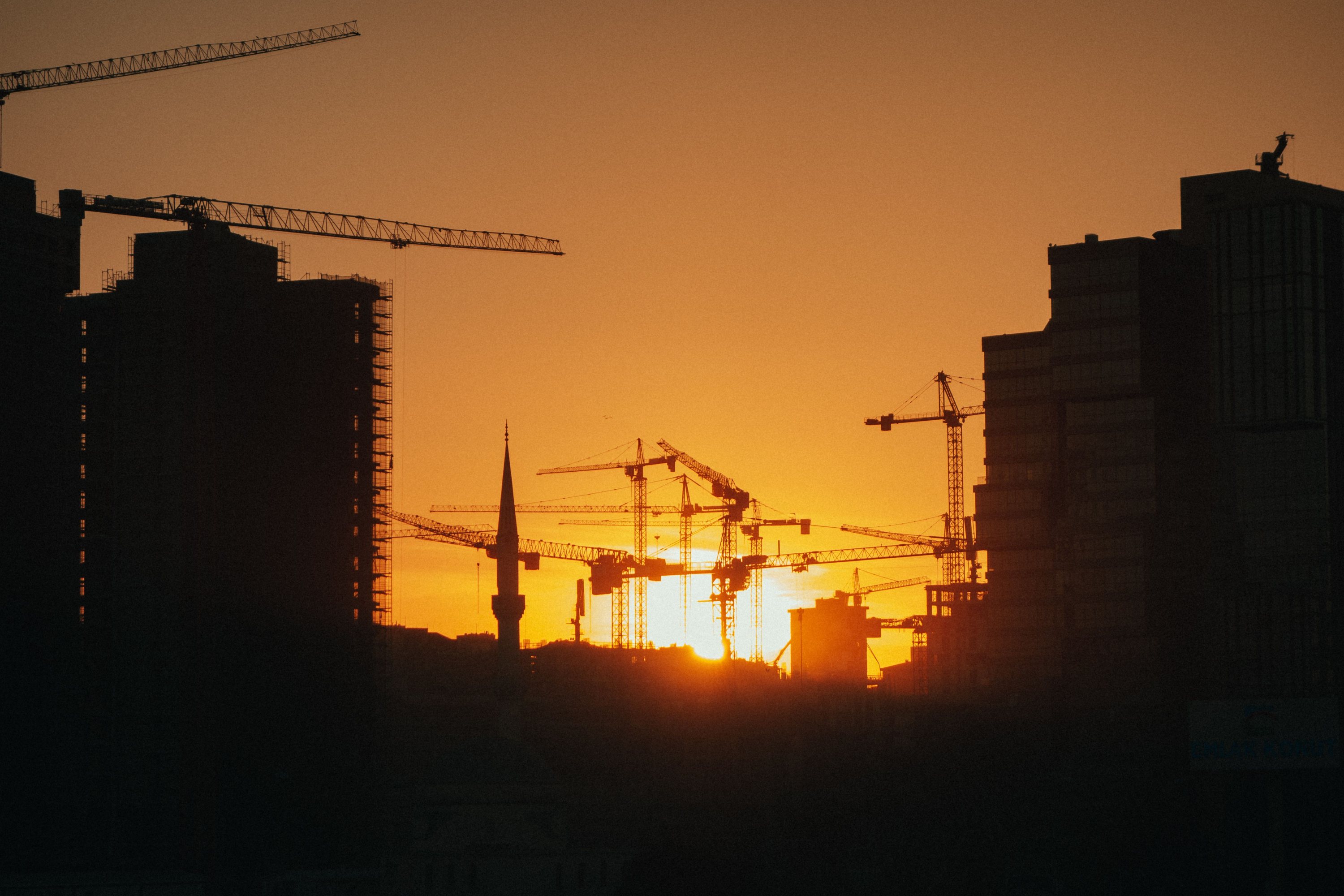 Grúas torre y edificios en construcción a contraluz al atardecer